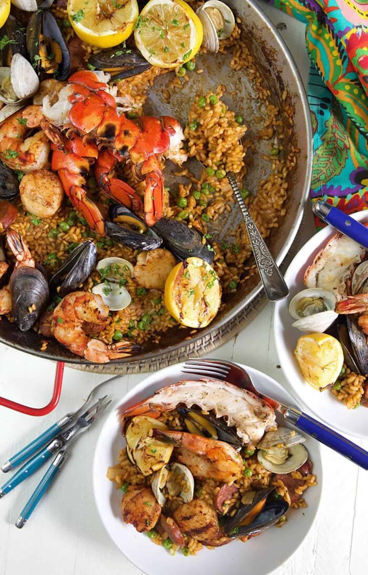 Grilled seafood paella in a paella pan with a bowl of seafood paella on a white background.