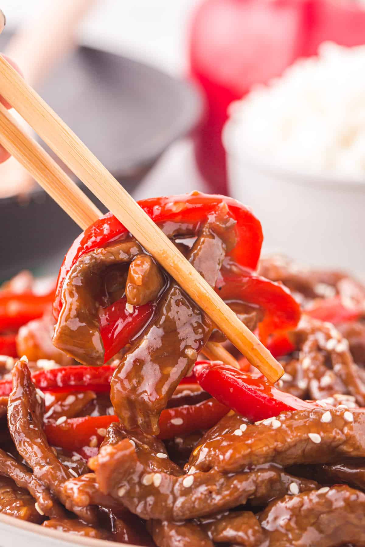 Chopsticks are lifting a bite of peppers and beef from a plate.