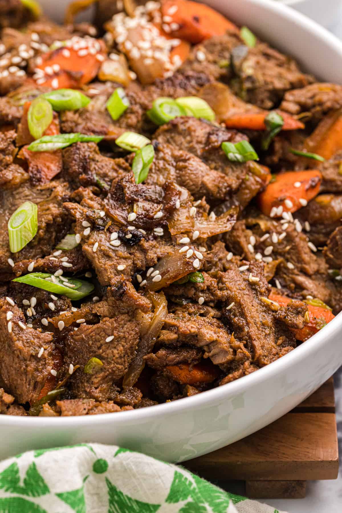 A white serving dish is filled with cooked beef and carrots. 