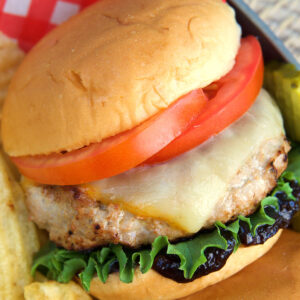 A turkey burger is topped with cheese, lettuce, and a tomato.