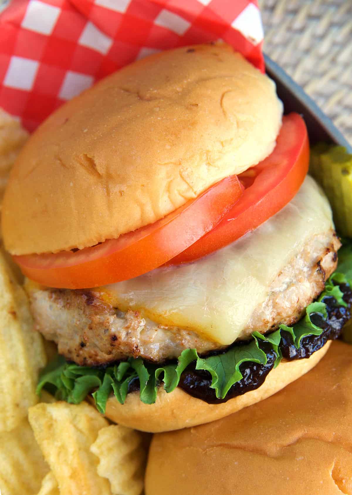 A turkey burger is topped with cheese, lettuce, and a tomato. 
