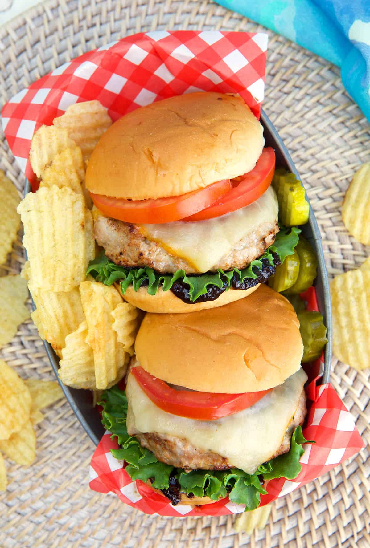 Two turkey burgers are plated with potato chips in a basket.