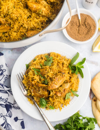 A single serving of chicken biryani is placed next to a skillet.