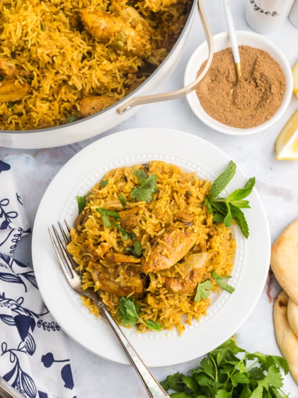 A single serving of chicken biryani is placed next to a skillet.