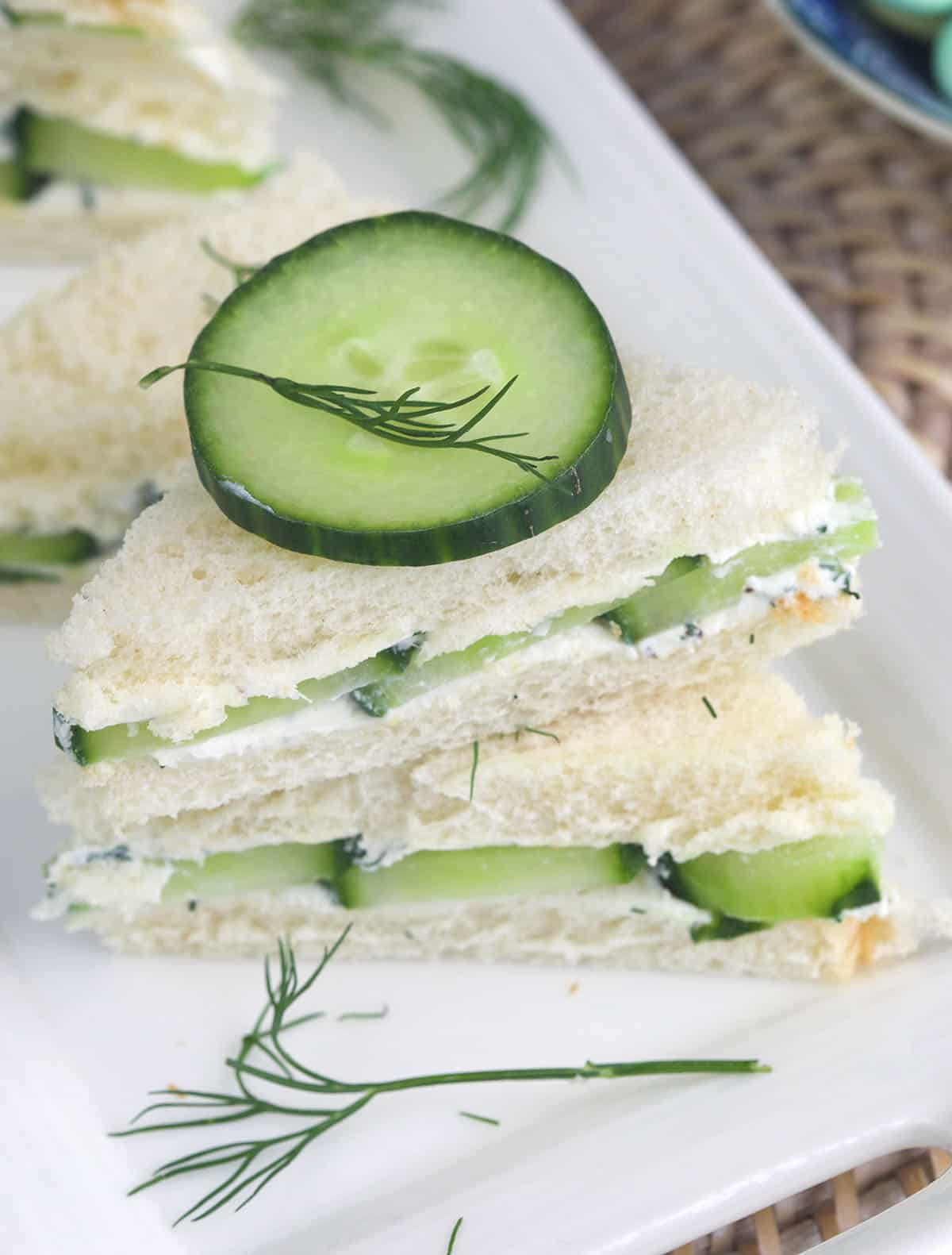 Two halves of a cucumber sandwich are stacked on a white plate.