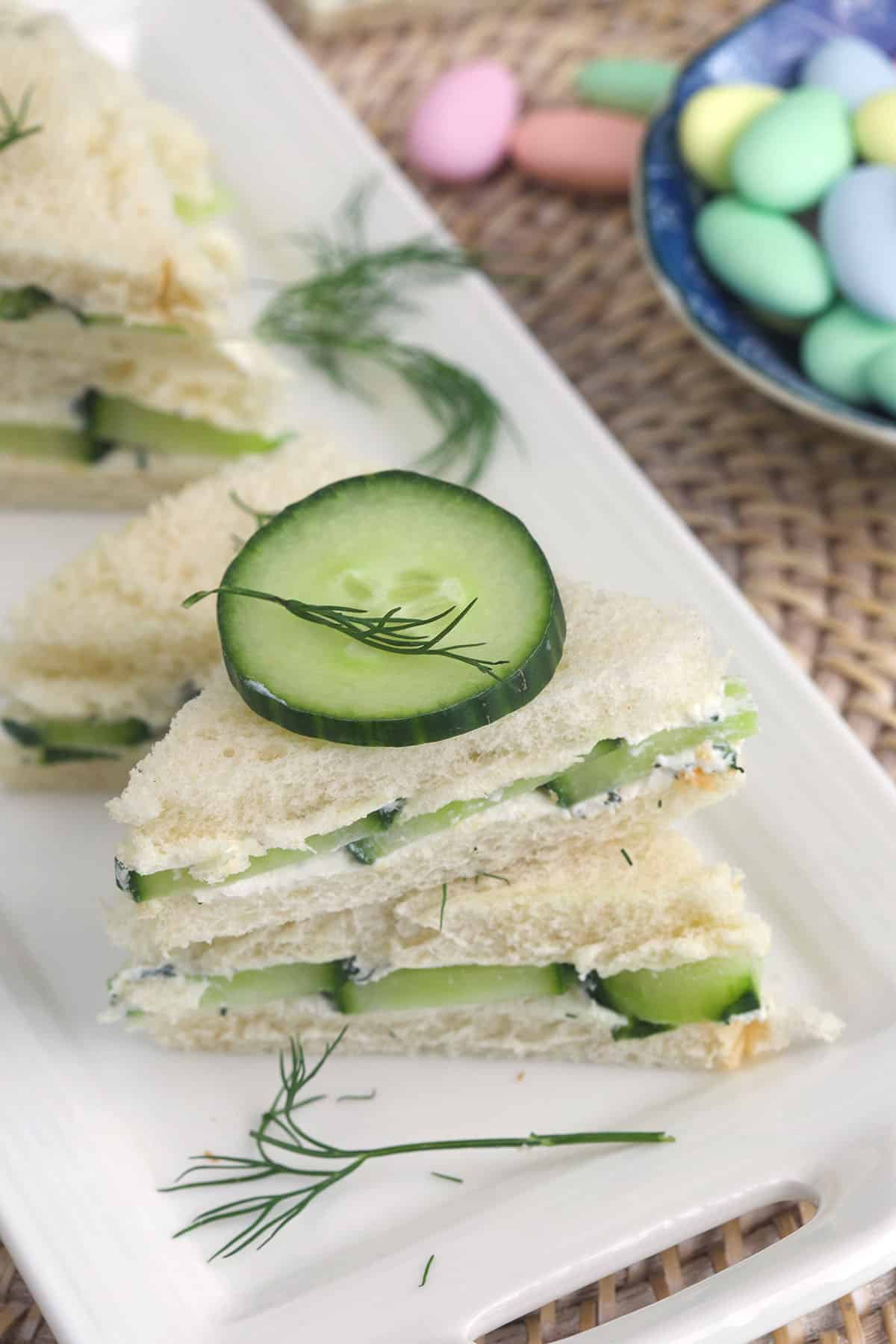 Stacked cucumber sandwiches are topped with cucumbers slices and fresh dill. 