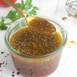 A spoon is lifting a small portion of Italian dressing out of a jar.