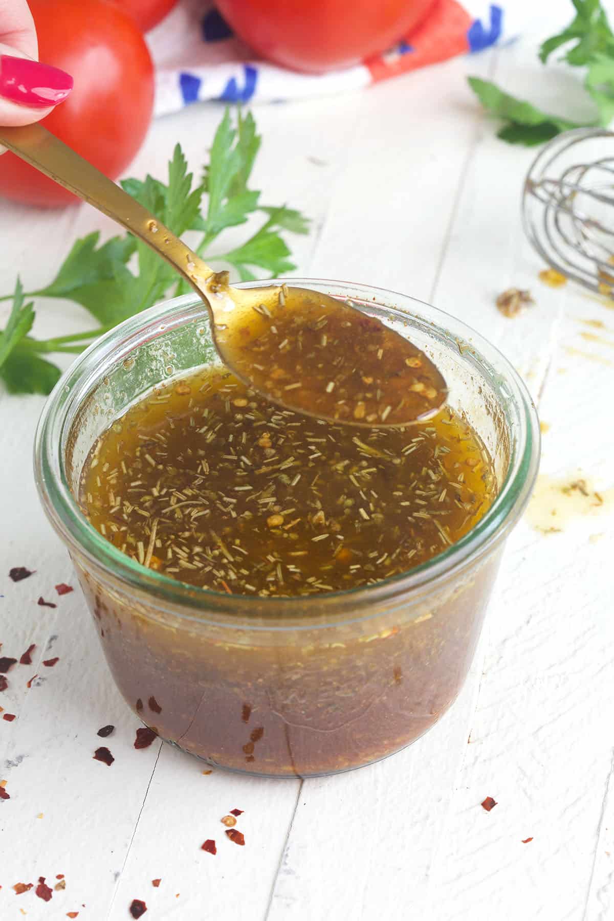 A spoon is lifting a small portion of Italian dressing out of a jar.