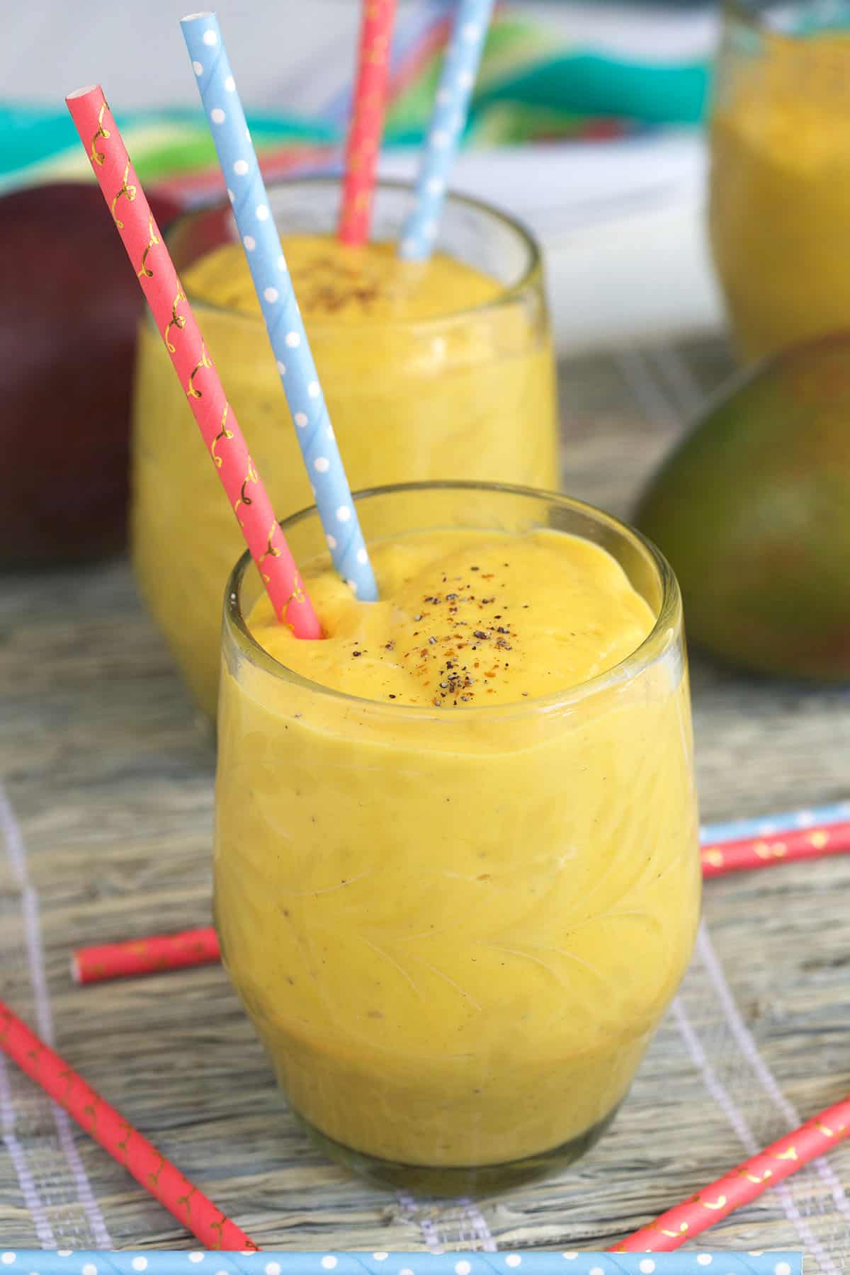 A glass of mango lassi has two straws placed in it.
