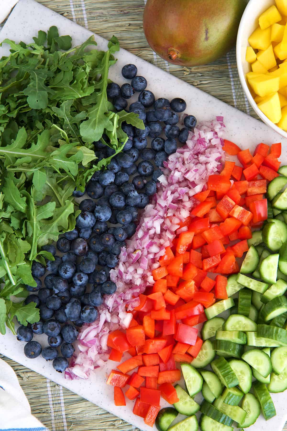The ingredients for mango salad are chopped and presented on a white plate. 