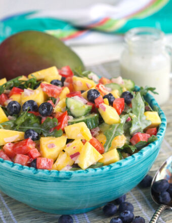 A blue salad bowl is filled with a tossed mango salad.