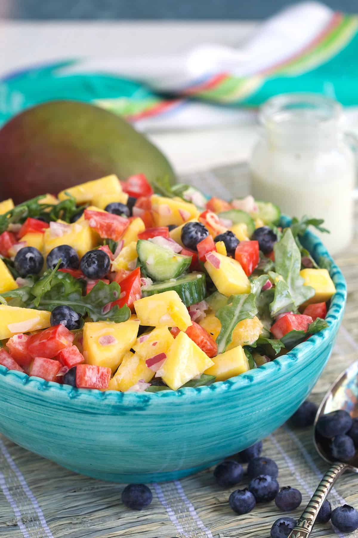 A blue salad bowl is filled with a tossed mango salad. 