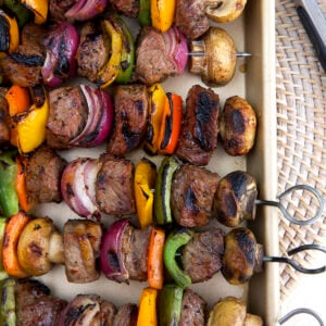 Steak shish kabobs are lined up on a large rimmed baking sheet.