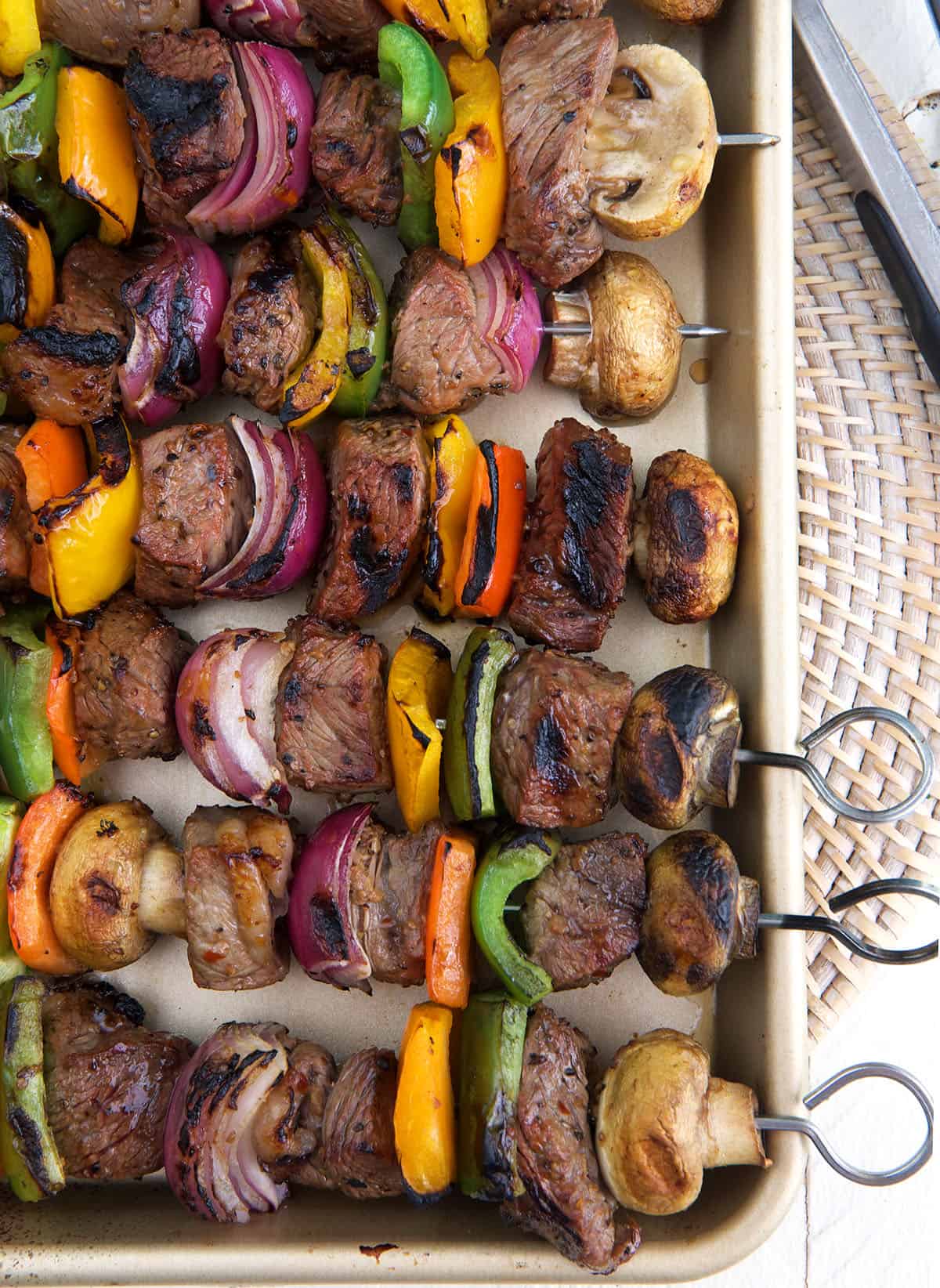 Steak shish kabobs are lined up on a large rimmed baking sheet.