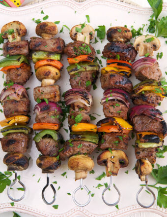 A white platter is topped with cooked steak shish kabobs and parsley.