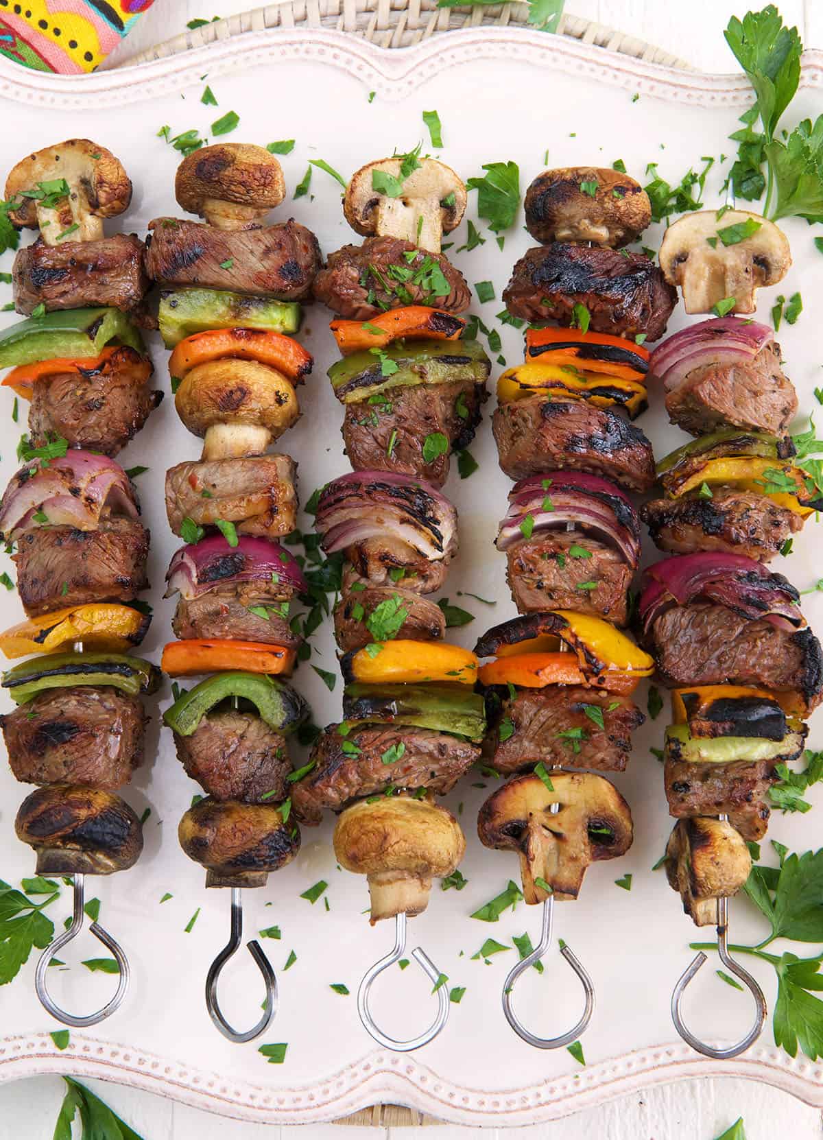 A white platter is topped with cooked steak shish kabobs and parsley.