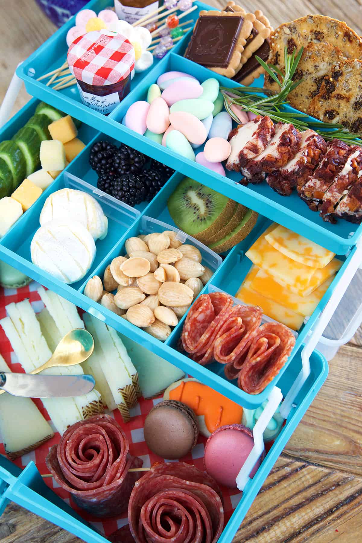 A blue tackle box is filled with cheeses, meats, and candies. 