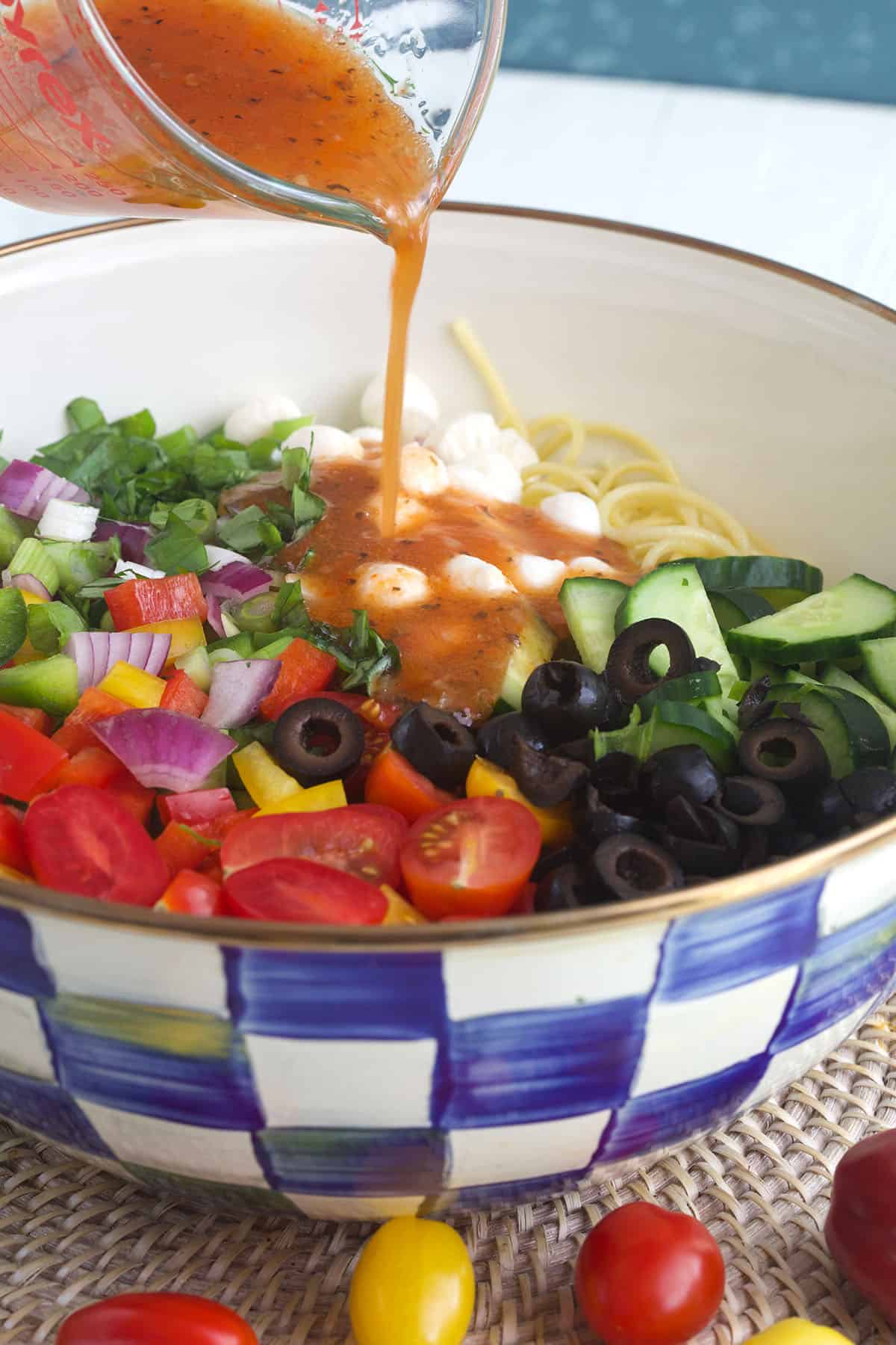 Dressing is being poured over spaghetti salad in a bowl. 