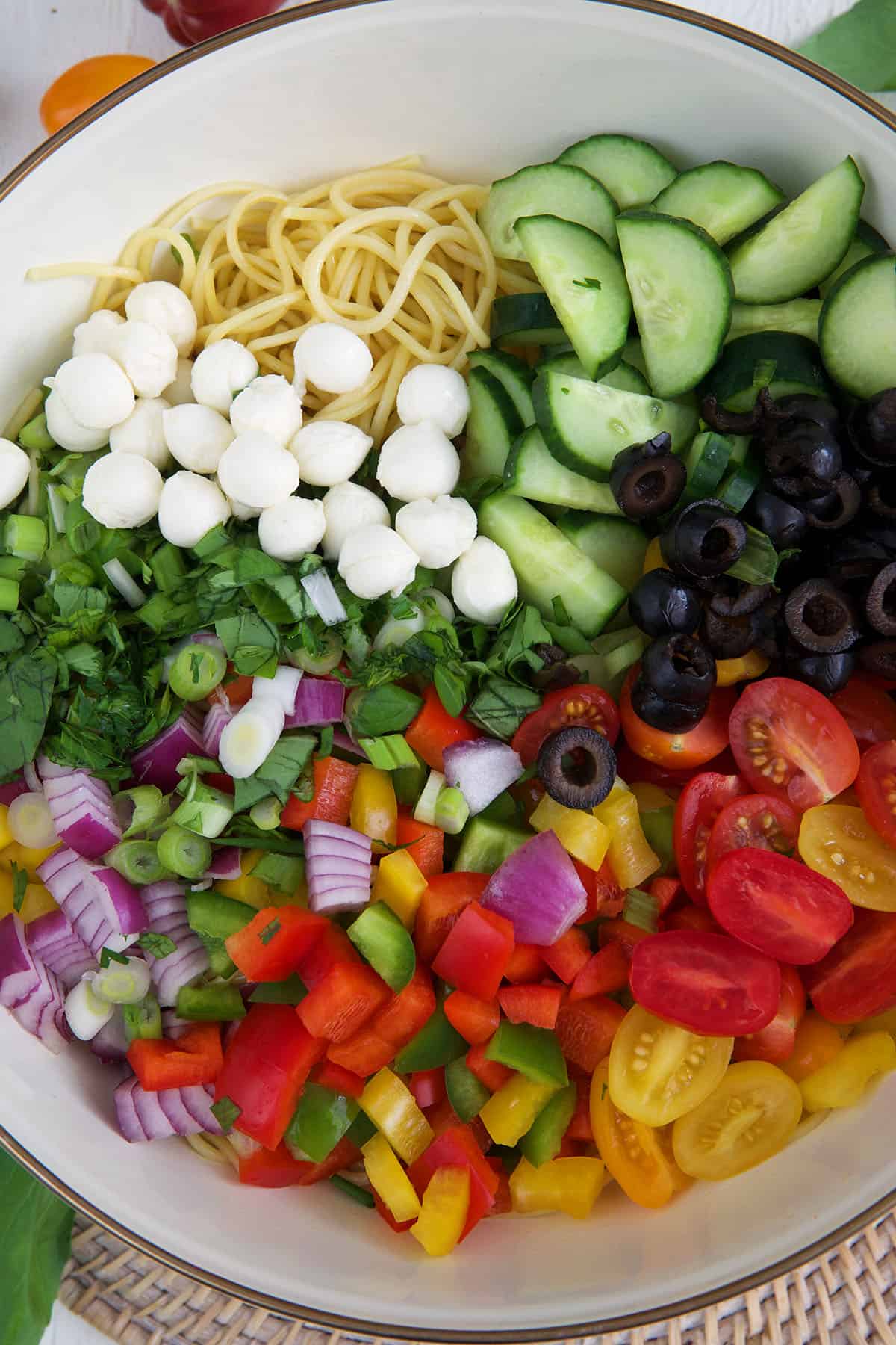 A large serving bowl is filled with the ingredients for spaghetti salad. 