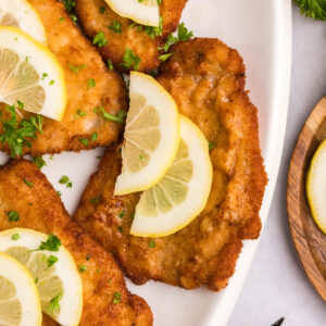 Several pieces of wiener schnitzel are plated with lemon slices.