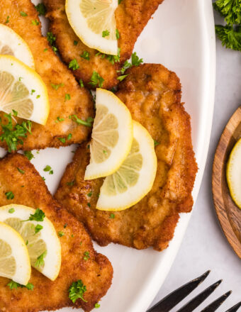 Several pieces of wiener schnitzel are plated with lemon slices.