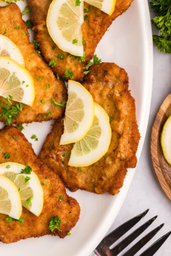 Several pieces of wiener schnitzel are plated with lemon slices.