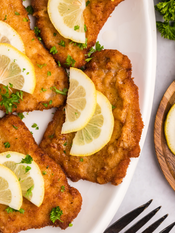 Several pieces of wiener schnitzel are plated with lemon slices.