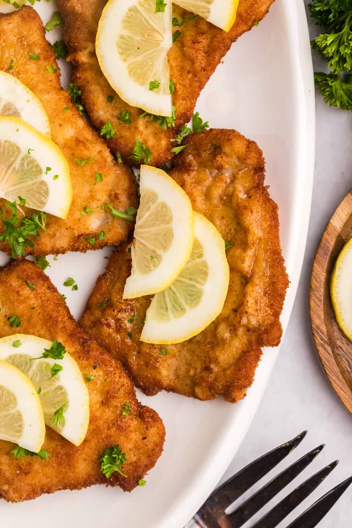 Several pieces of wiener schnitzel are plated with lemon slices. 
