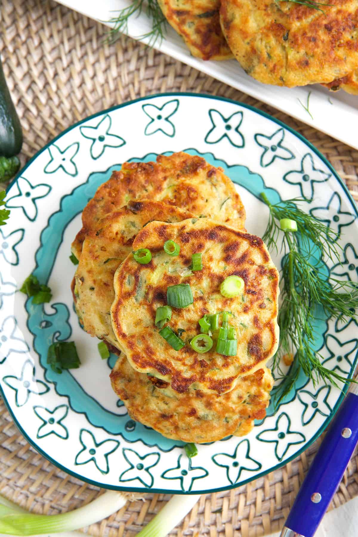 A plate of zucchini fritters is garnished with green onions. 