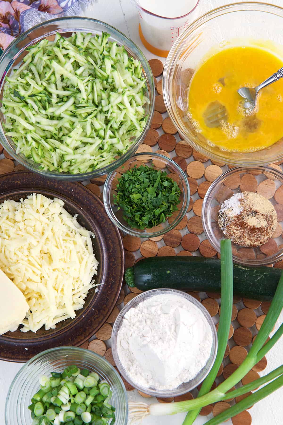 The ingredients for zucchini fritters are placed on a wooden surface.
