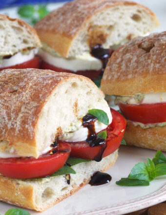 Balsamic glaze is drizzle in the middle of a halved caprese sandwich.