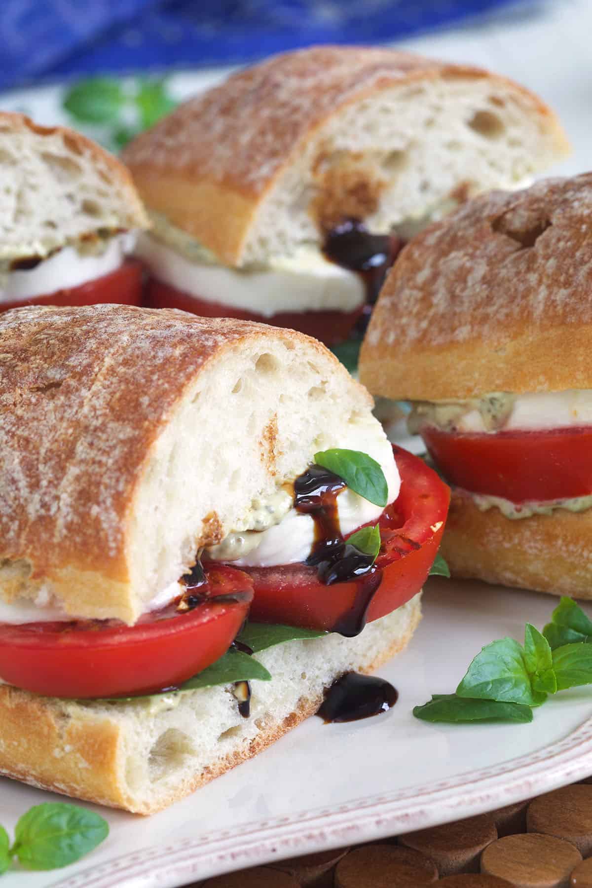 Balsamic glaze is drizzle in the middle of a halved caprese sandwich. 