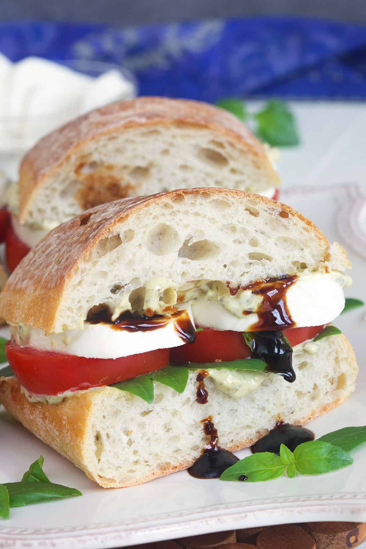 A caprese sandwich has been cut in half and is served with balsamic reduction.
