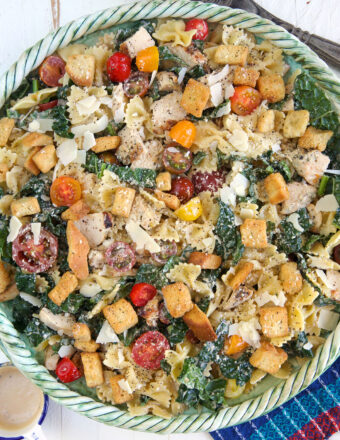 Chicken Caesar Pasta Salad in a green serving bowl with a blue napkin underneath.