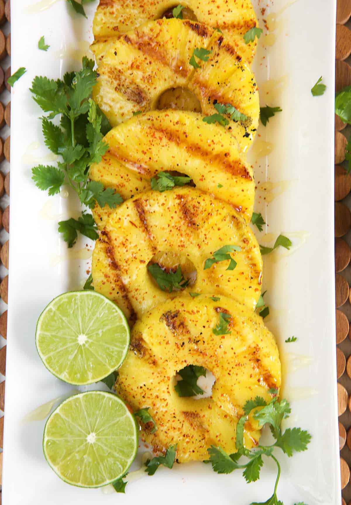 Grilled pineapple on a white platter with sliced lime and chopped cilantro