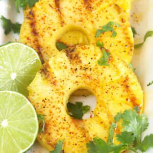 Three slices of grilled pineapple with cilantro sprigs and two lime slices.