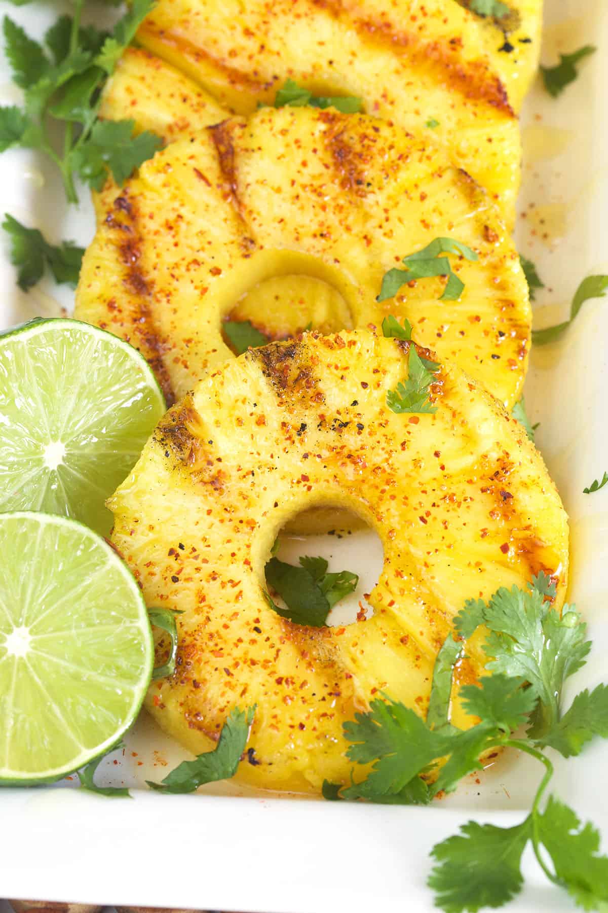 Three slices of grilled pineapple with cilantro sprigs and two lime slices.