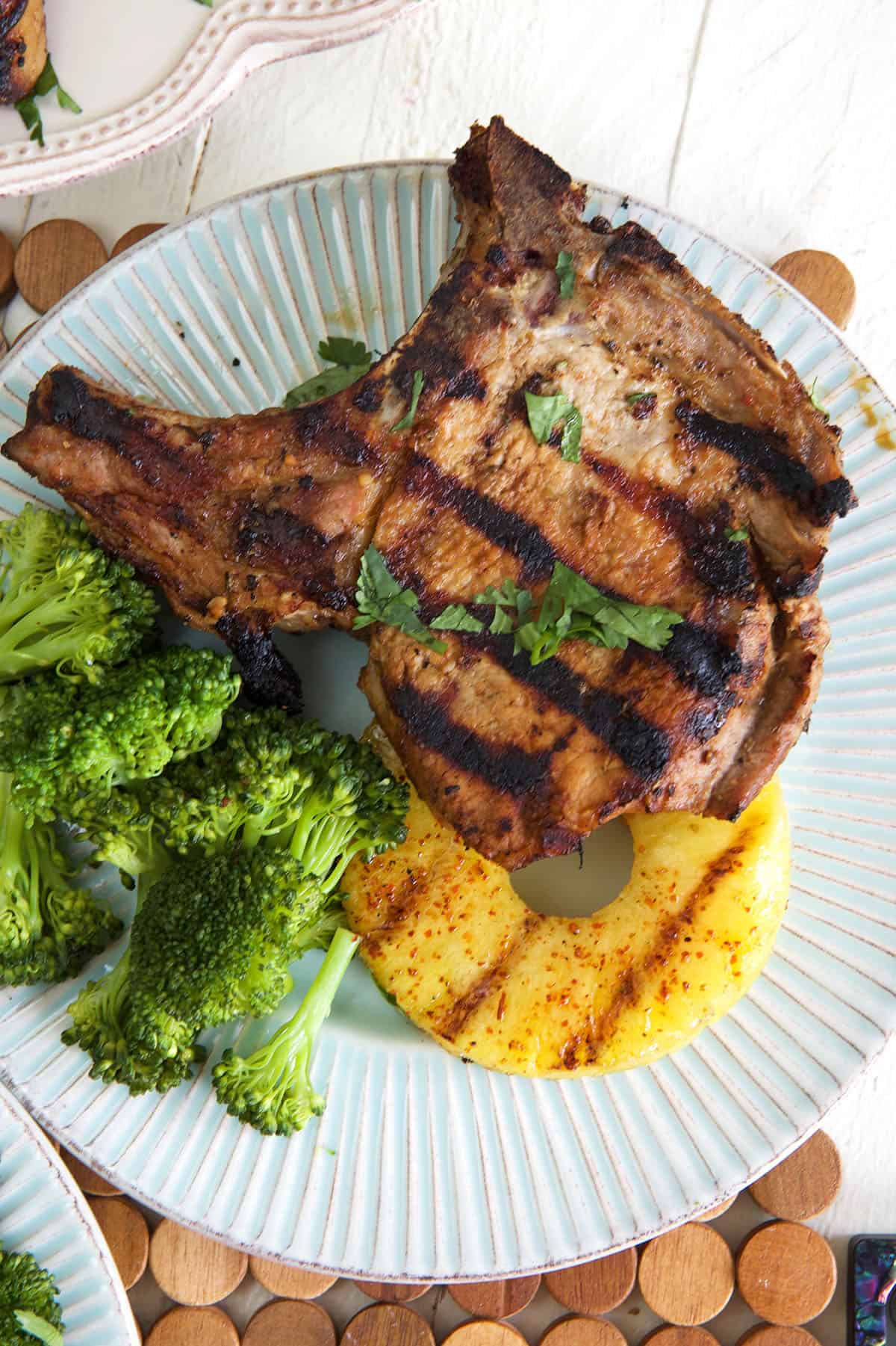 Pineapple and broccoli is placed next to a grilled pork chop. 