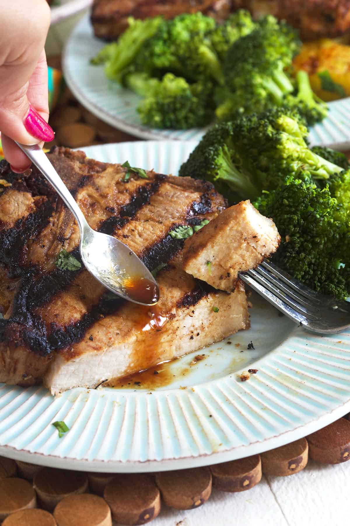 A spoon is drizzling some brown sauce onto a pork chop. 