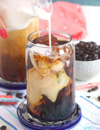 Creamer being poured into a glass of iced coffee.