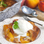 A scoop of vanilla ice cream is placed on top of a serving of peach cobbler.