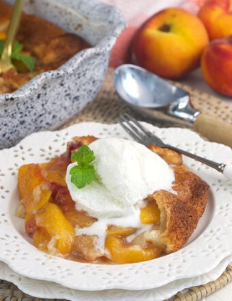 A scoop of vanilla ice cream is placed on top of a serving of peach cobbler.