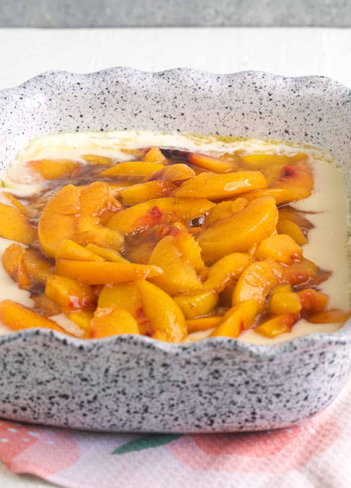Peaches are placed in the middle of a casserole dish and are surrounded by batter. 