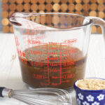 A whisk is placed next to marinade and a side of brown sugar.