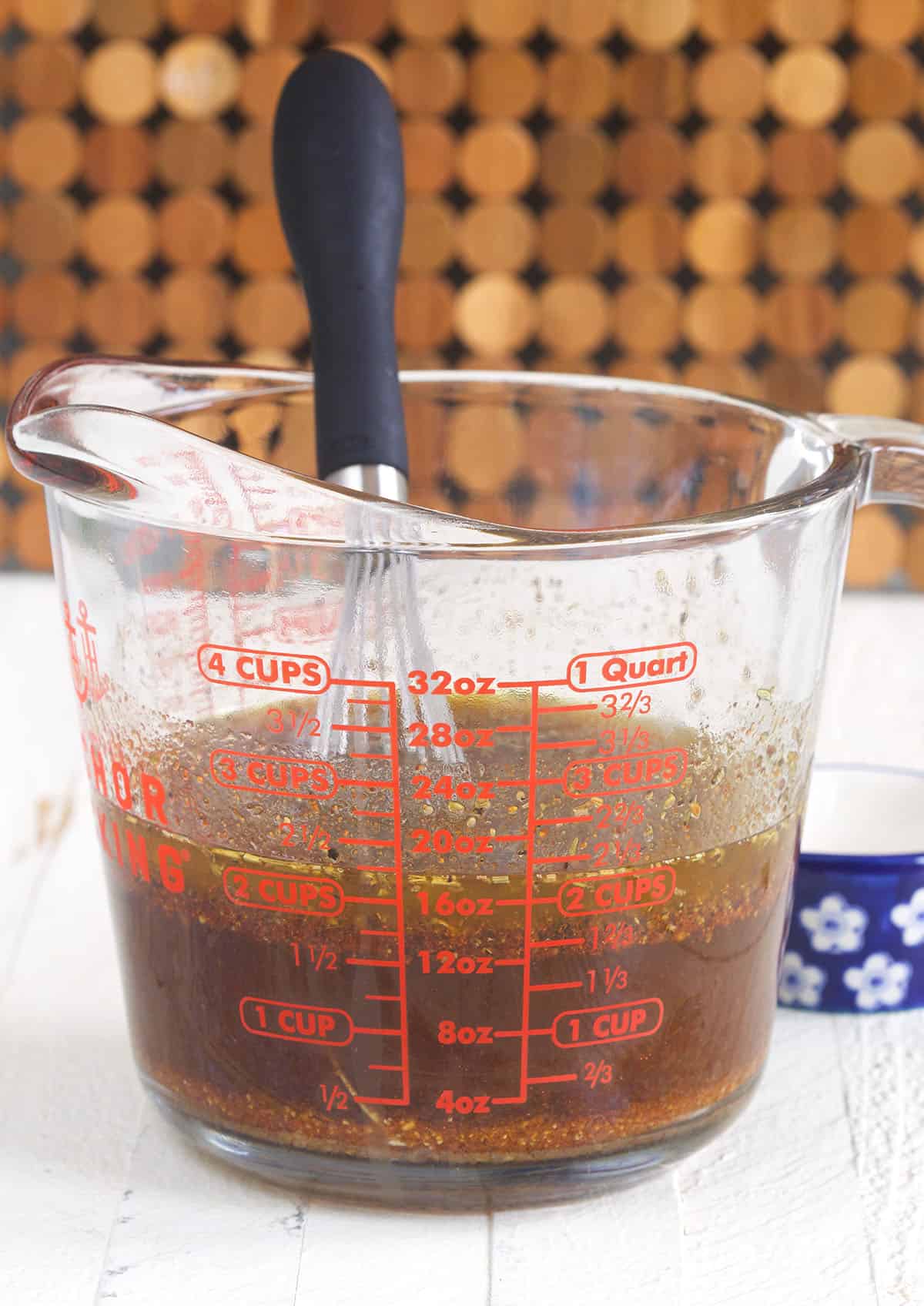 A whisk is stirring ingredients together in a measuring glass. 