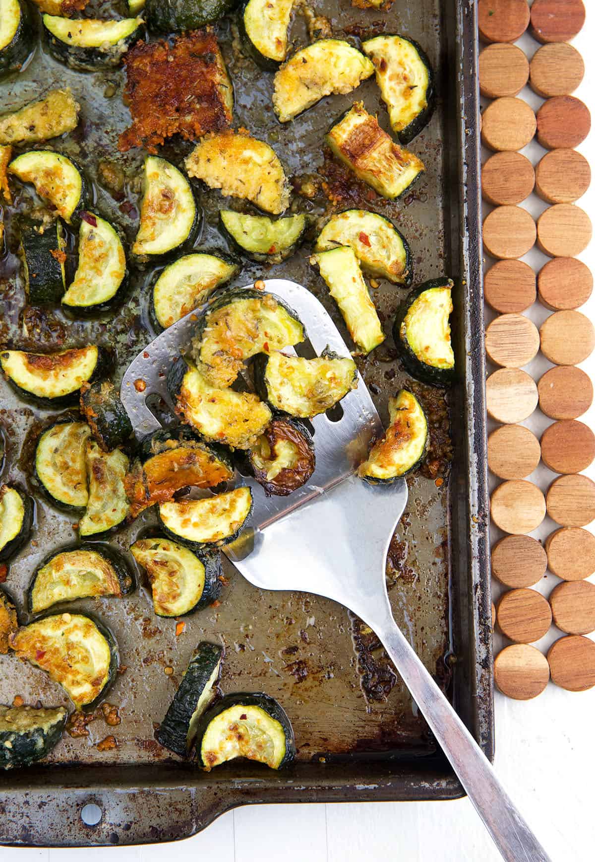A spatula is lifting some roasted zucchini from a baking sheet.