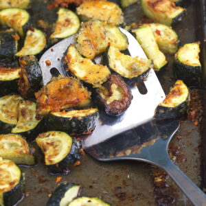 A spatula is placed on a baking sheet full of cooked zucchini.