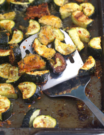 A spatula is placed on a baking sheet full of cooked zucchini.