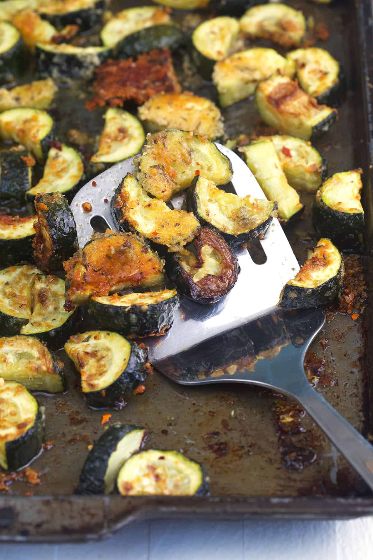 A spatula is placed on a baking sheet full of cooked zucchini. 