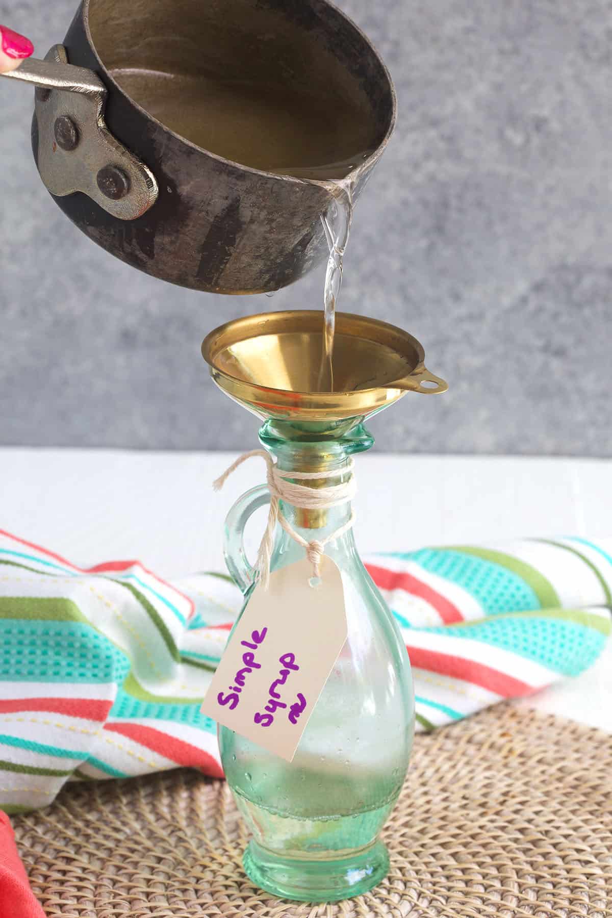 Simple syrup being poured into a gold funnel into a glass bottle.